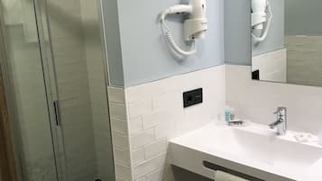 Un baño moderno con cabina de ducha de vidrio, un lavabo blanco con una toalla y un secador de pelo montado en la pared.