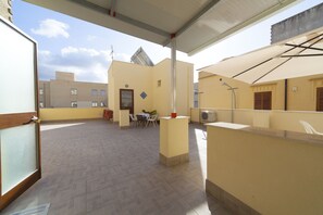 A rooftop terrace with a table and chairs, a small garden, and a building with a sloped roof.