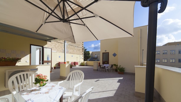 A covered outdoor patio with white chairs and a table, featuring a tiled floor and a large umbrella. - Sole di Trapani (Trapani)