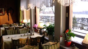Un restaurant avec des tables et des chaises en bois, des plantes en pot et une vue sur un paysage enneigé, visible à travers de grandes fenêtres.