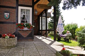Un café avec des tables à l’extérieur, une enseigne indiquant qu’il s’agit d’un café, et des jardinières fixées au mur.