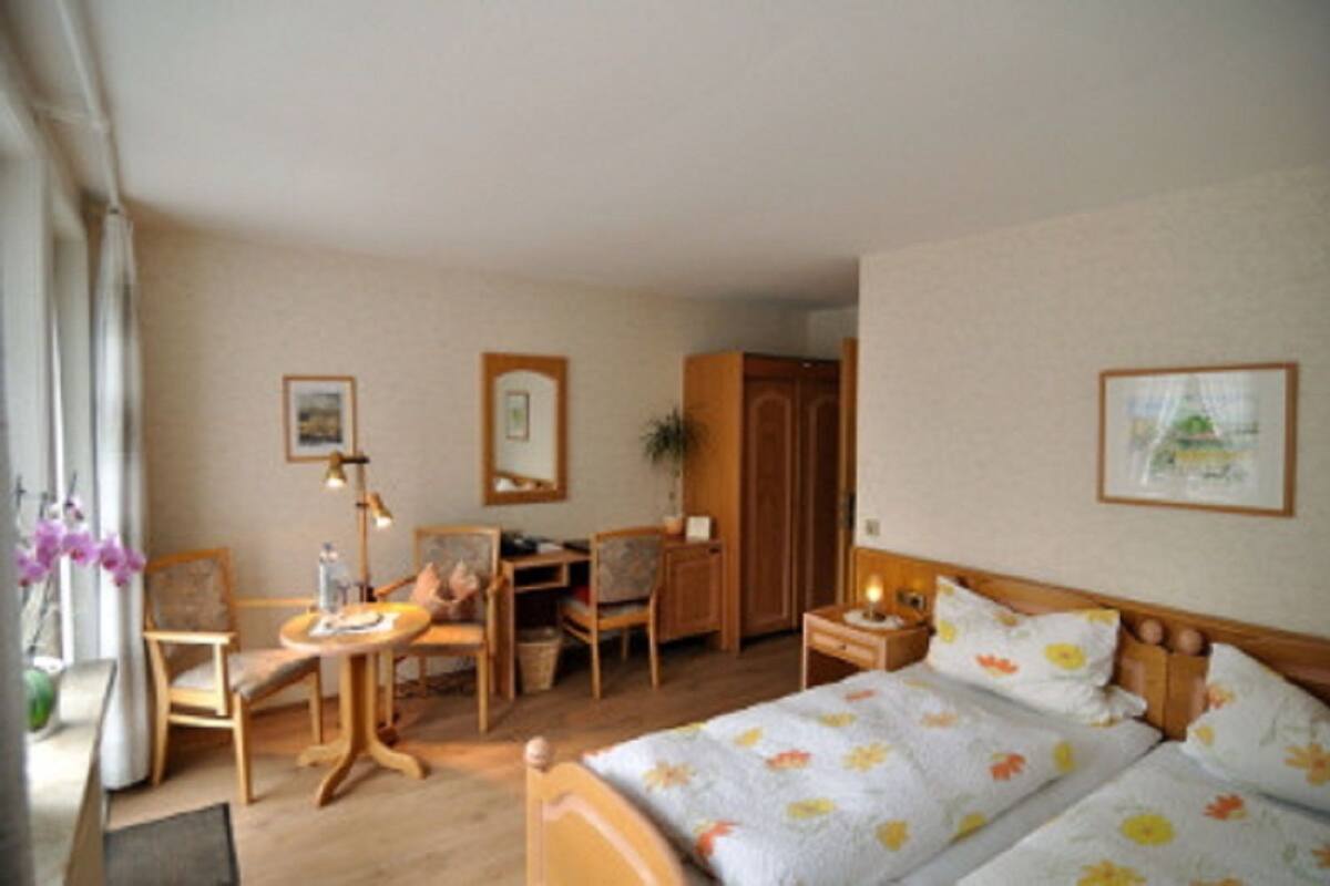 Una habitación de hotel con cama, escritorio, silla, mesita de noche y ventana con cortinas.
