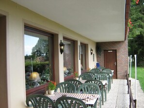 An outdoor patio with multiple tables and chairs, large windows, and a brick wall. - Land-gut-hotel Landhaus Heidehof (Clenze)