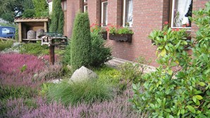 Un jardin où l’on trouve une variété de plantes, une structure en bois et un bâtiment en briques doté de fenêtres.