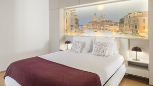 A modern hotel room with a large bed, a view of Venice through a window, and a nightstand with a lamp. - Baía I, apartment with luxury design (Funchal)