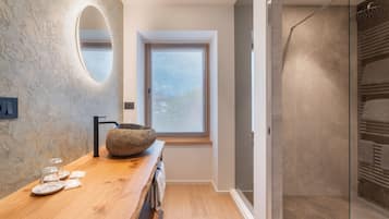 Un baño moderno con tocador de madera, un espejo ovalado grande y un cuenco de piedra como elemento central.