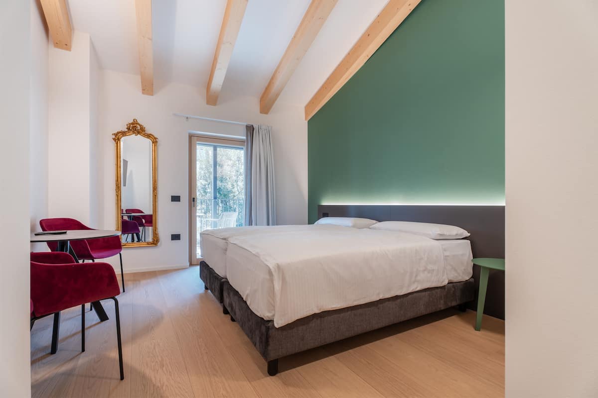 A modern bedroom with a bed, a desk with a chair, a large mirror, and a view of the outdoors.