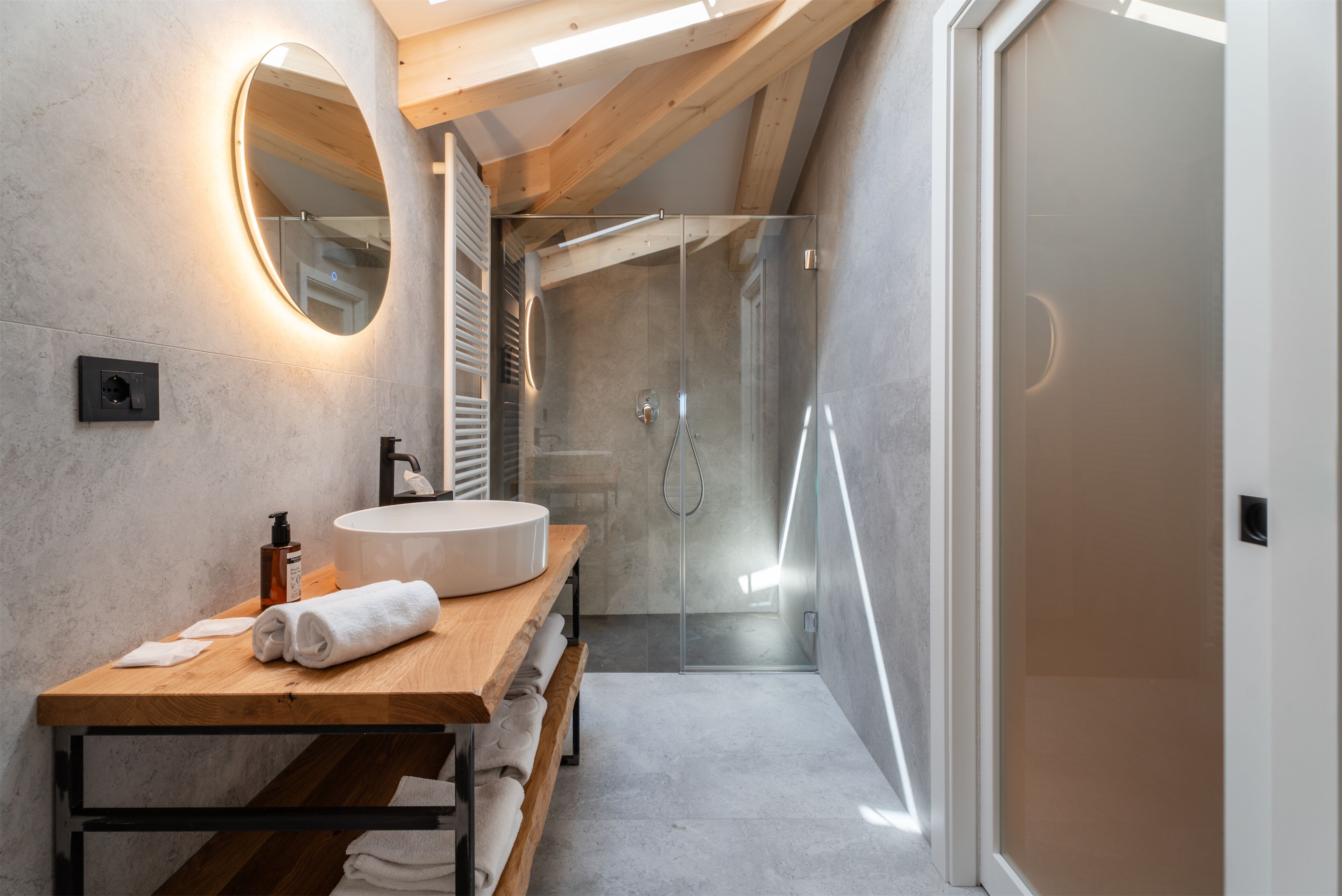 A modern bathroom with a wooden vanity, a large mirror, and a glass-enclosed shower.