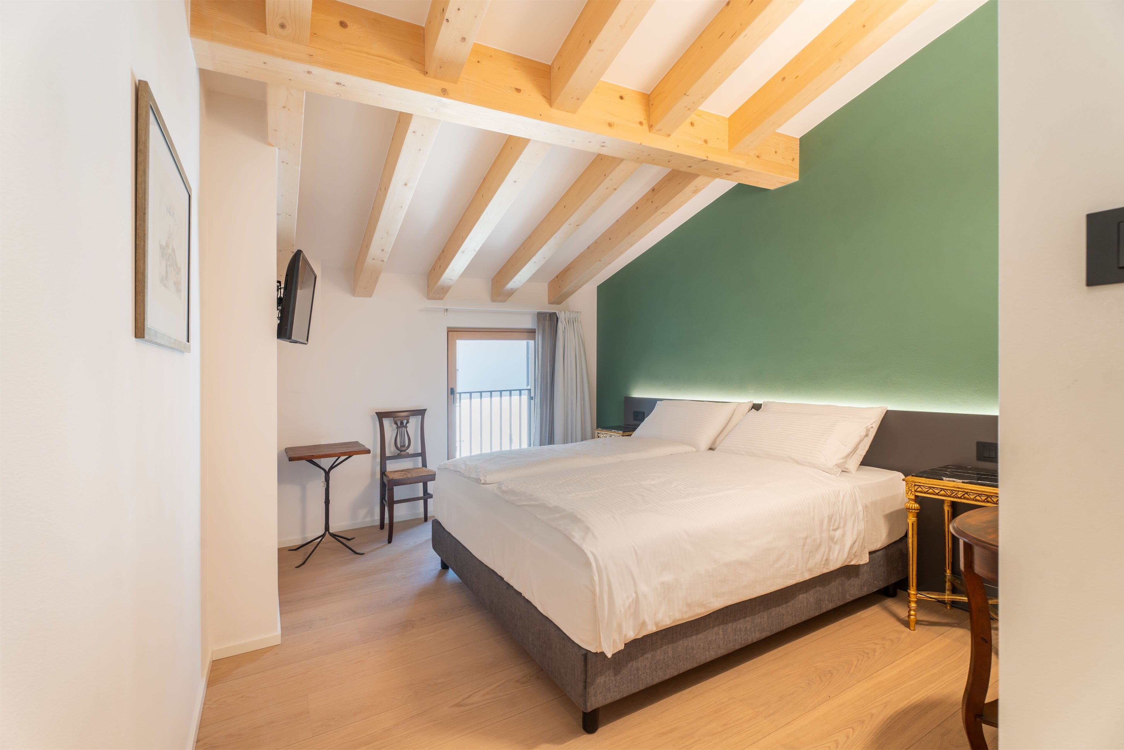 Un dormitorio con una cama grande, vigas de madera en el techo, una mesita y una silla.