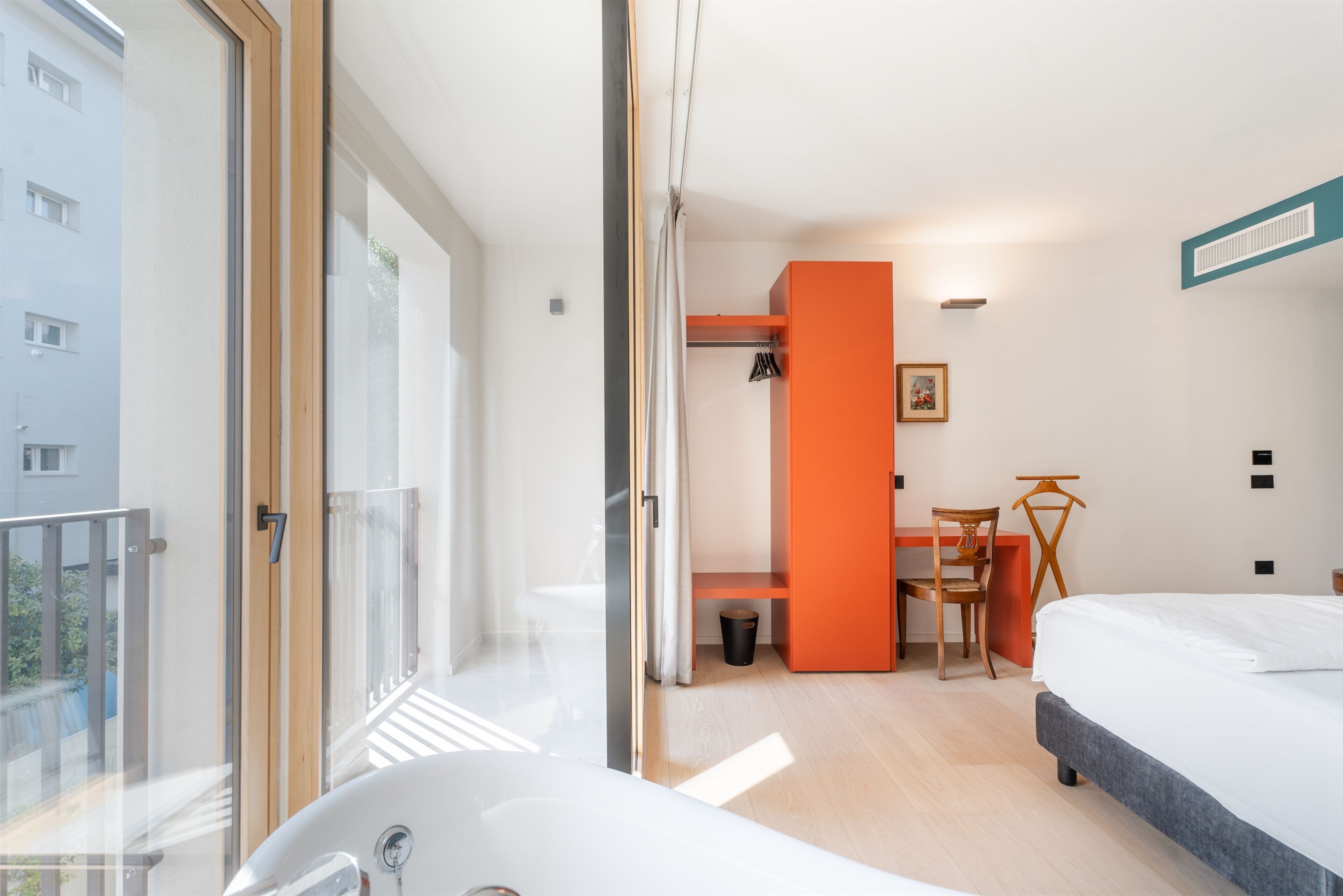 Een moderne hotelkamer met een groot raam, een badkuip, een bed, een bureau en een oranje accentmuur.