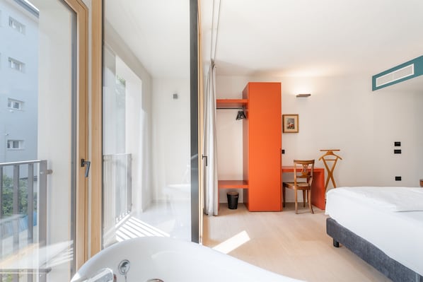 A modern hotel room with a large window, a bathtub, a bed, a desk, and an orange accent wall. - Locanda Restel de Fer (Riva del Garda)