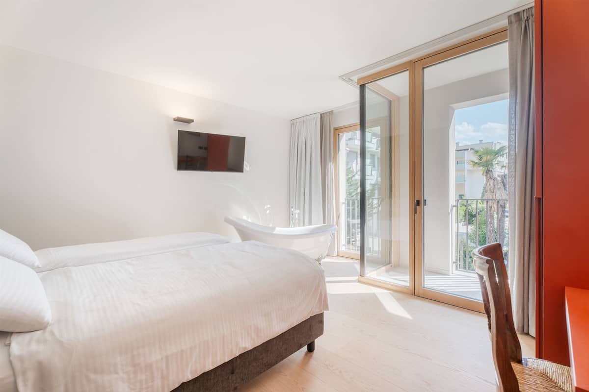A bedroom with a large bed, a bathtub, and a sliding glass door leading to a balcony.