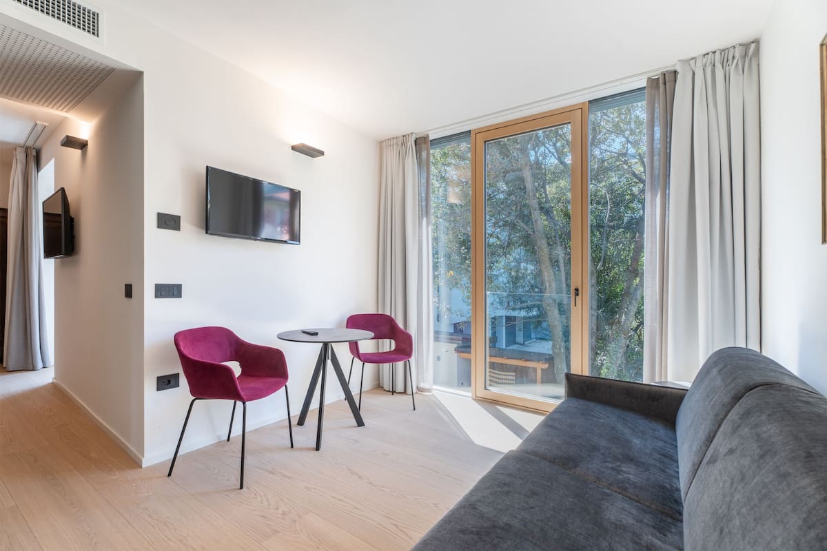 A modern living room with a grey sofa, a TV mounted on the wall, and a glass door leading to an outdoor area.