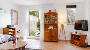 Een woonkamer met een houten kast, een televisie, een tafel met een vaas, en een raam met uitzicht op groen.