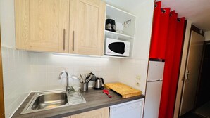 Cozinha com armários de madeira, pia de aço inoxidável, micro-ondas, torradeira e cortina vermelha.