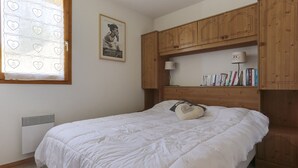 A bedroom with a bed, wooden cabinets, a radiator, a framed picture, and a window with heart-shaped curtains. - Charming 4-room apartment, sleeps 8, near slopes, parking, WIFI (Peisey-Vallandry)