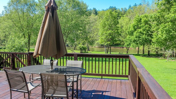 Une terrasse en bois avec une table et des chaises, donnant sur un étang et des arbres.