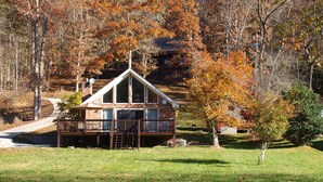 Une cabane dotée d’une terrasse, entourée d’arbres aux feuilles d’automne.