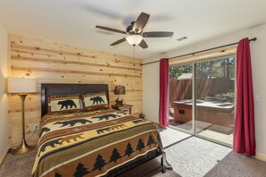 A bedroom with a bed, a ceiling fan, a nightstand, a lamp, a window with red curtains, and a sliding glass door leading to an outdoor area.