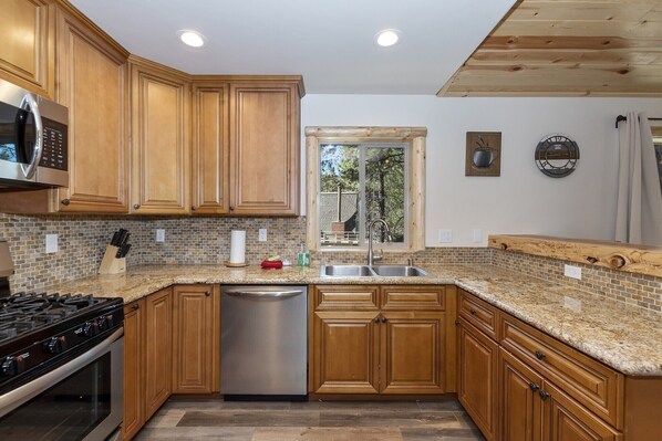 A kitchen with wooden cabinets, a stainless steel dishwasher, a granite countertop, and a view through a window.