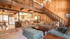 A spacious living area with a high ceiling, wooden beams, a staircase, and a cozy seating arrangement.