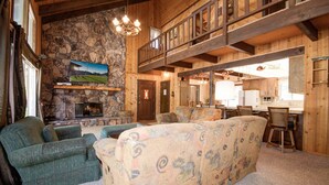 A cozy lodge interior with a stone fireplace, wooden furniture, and a kitchen area.