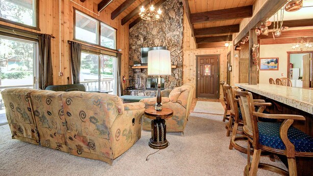 A cozy interior with a stone fireplace, wooden beams, and a dining area with chairs and a table.