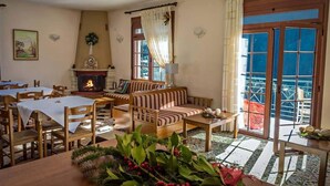 A cozy room with a fireplace, a sofa, and a dining area with tables. - To Kallion (Karpenisi)