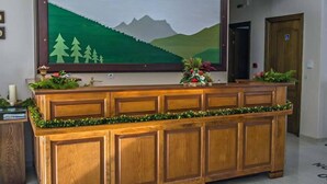A reception desk with a framed landscape painting, a wooden counter, and decorative greenery. - To Kallion (Karpenisi)