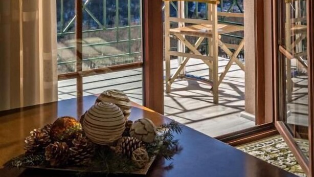 A room with a large window offering a view of snow-capped mountains and a balcony with wooden chairs. - To Kallion (Karpenisi)