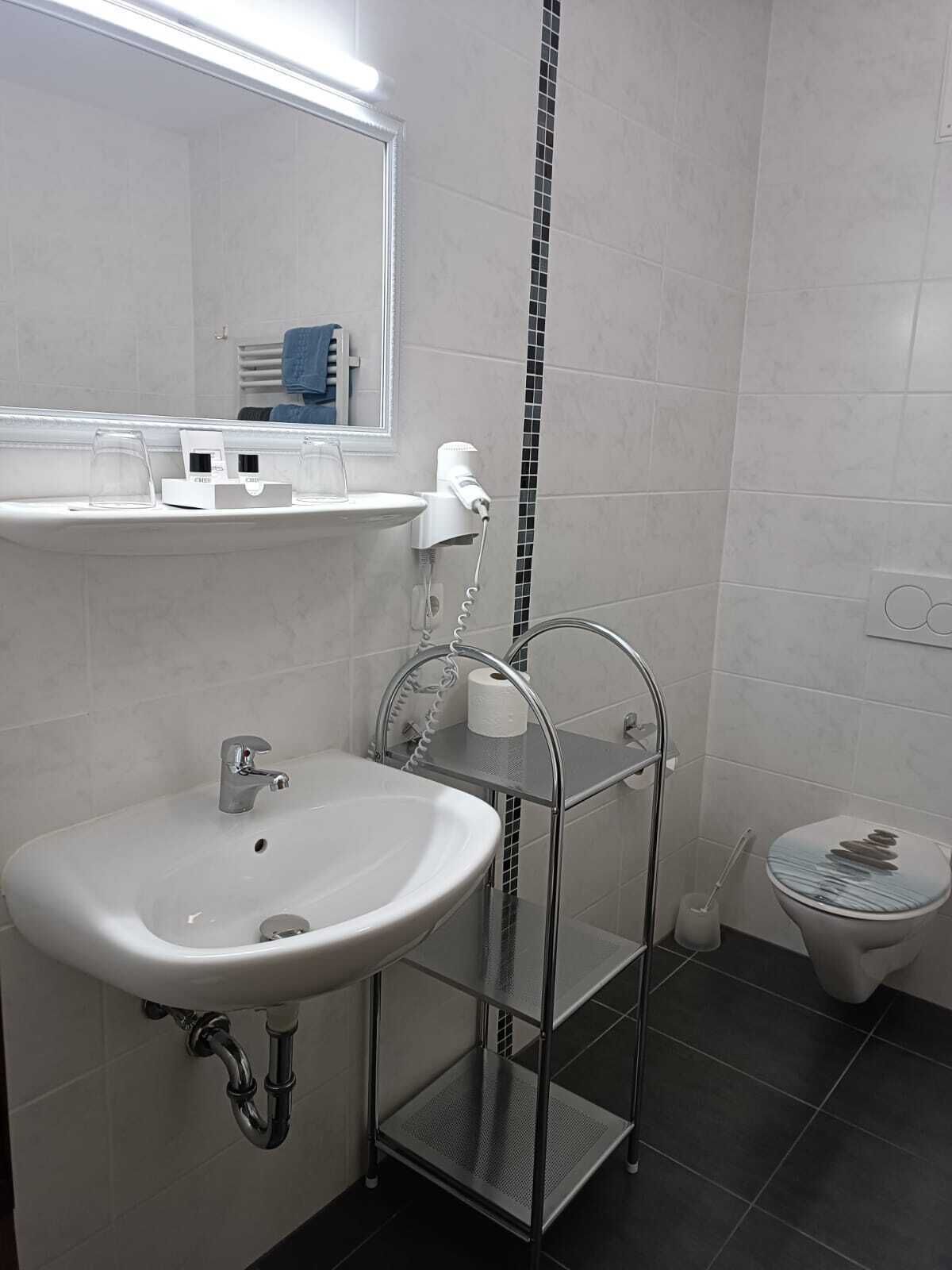 A modern bathroom with a white sink, a mirror, a towel rack, and a toilet.