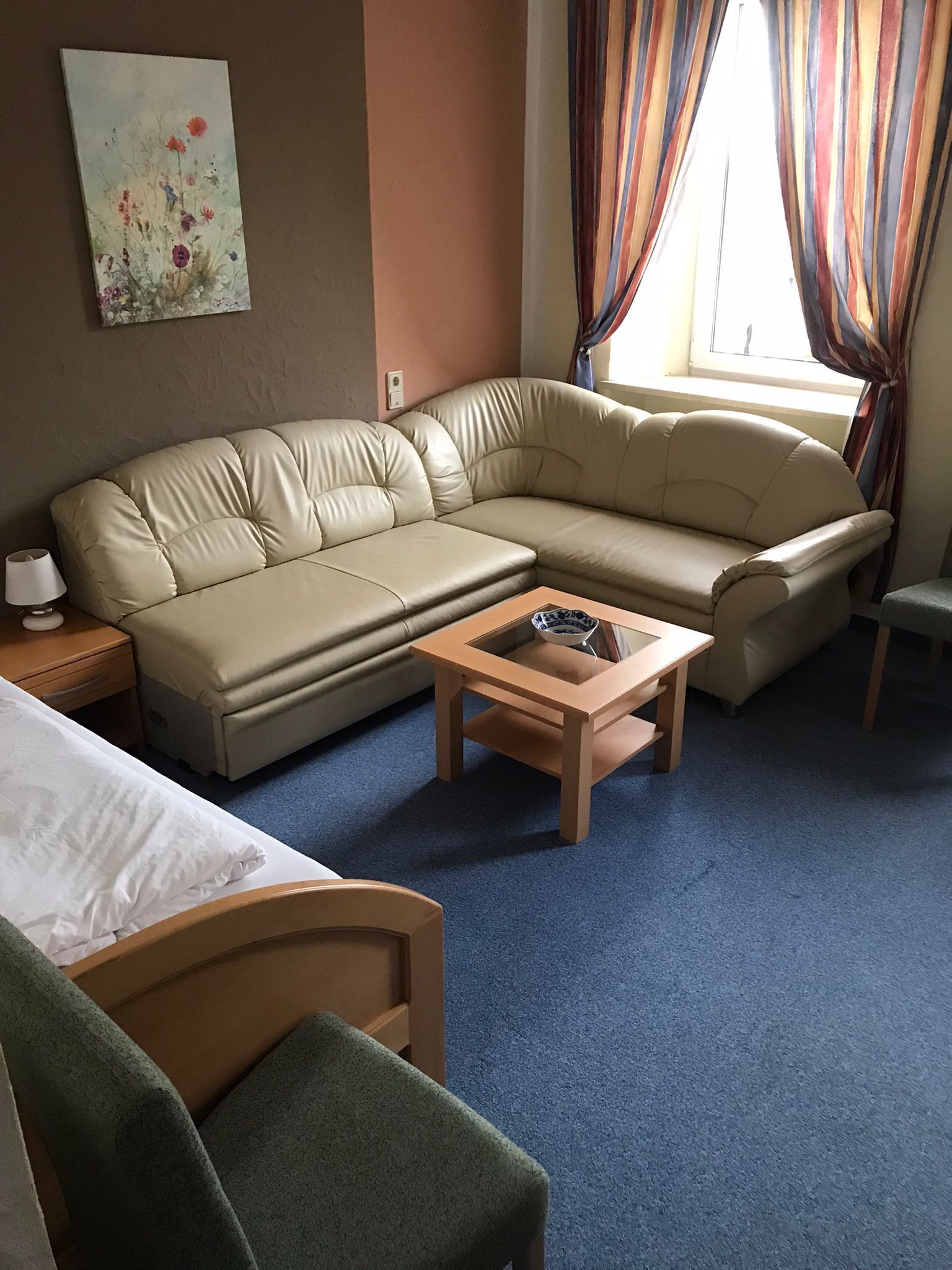 Ein Hotelzimmer mit einem beigefarbenen Sofa, einem Holztisch, einem kleinen Nachttisch und einem grünen Sessel.