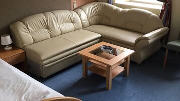 Ein Hotelzimmer mit einem beigefarbenen Sofa, einem Holztisch, einem kleinen Nachttisch und einem grünen Sessel.