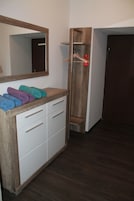 Casa de banho com toucador de madeira, espelho e prateleira com toalhas.
