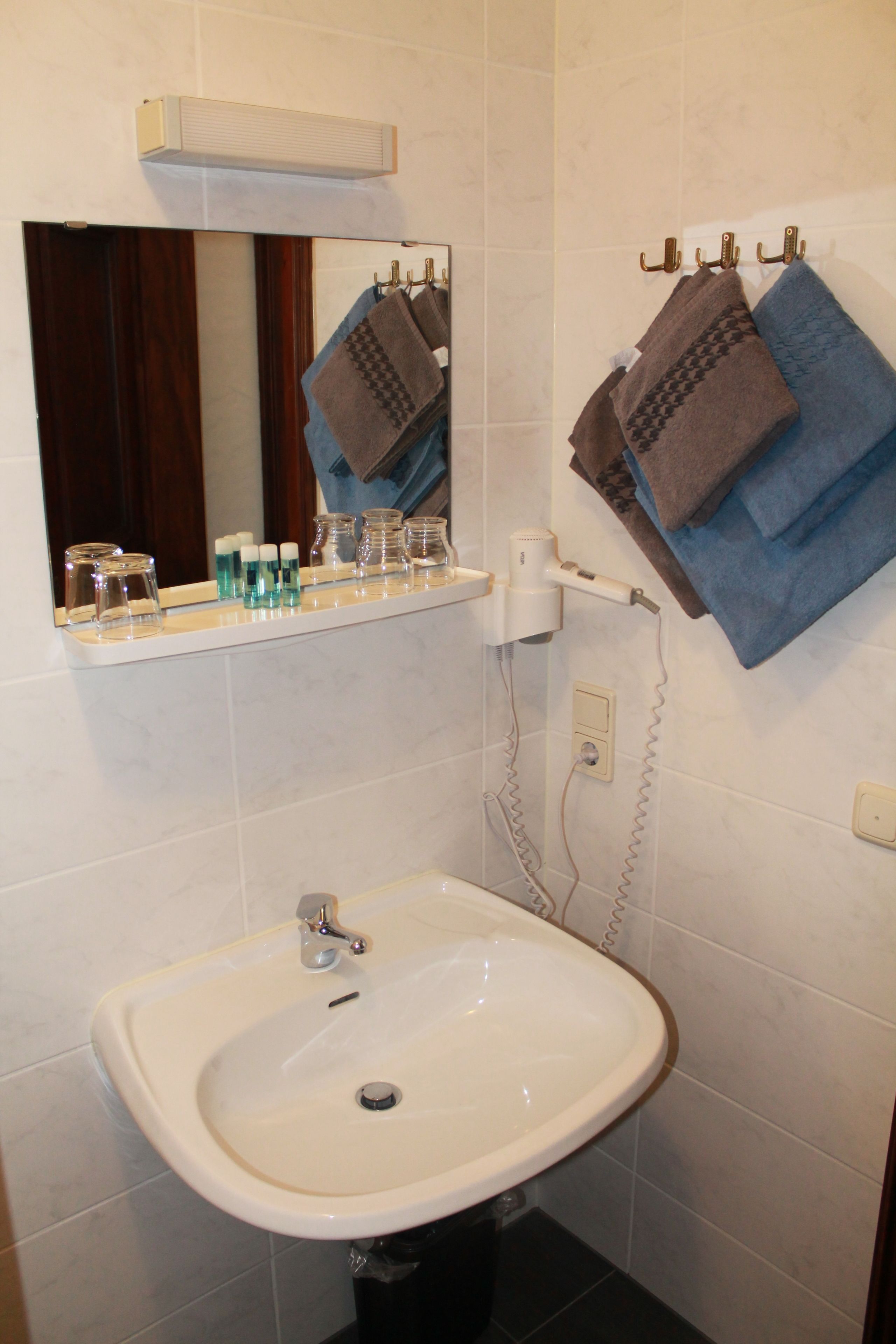 Une salle de bain avec un lavabo blanc, un miroir et un porte-serviettes avec des serviettes.