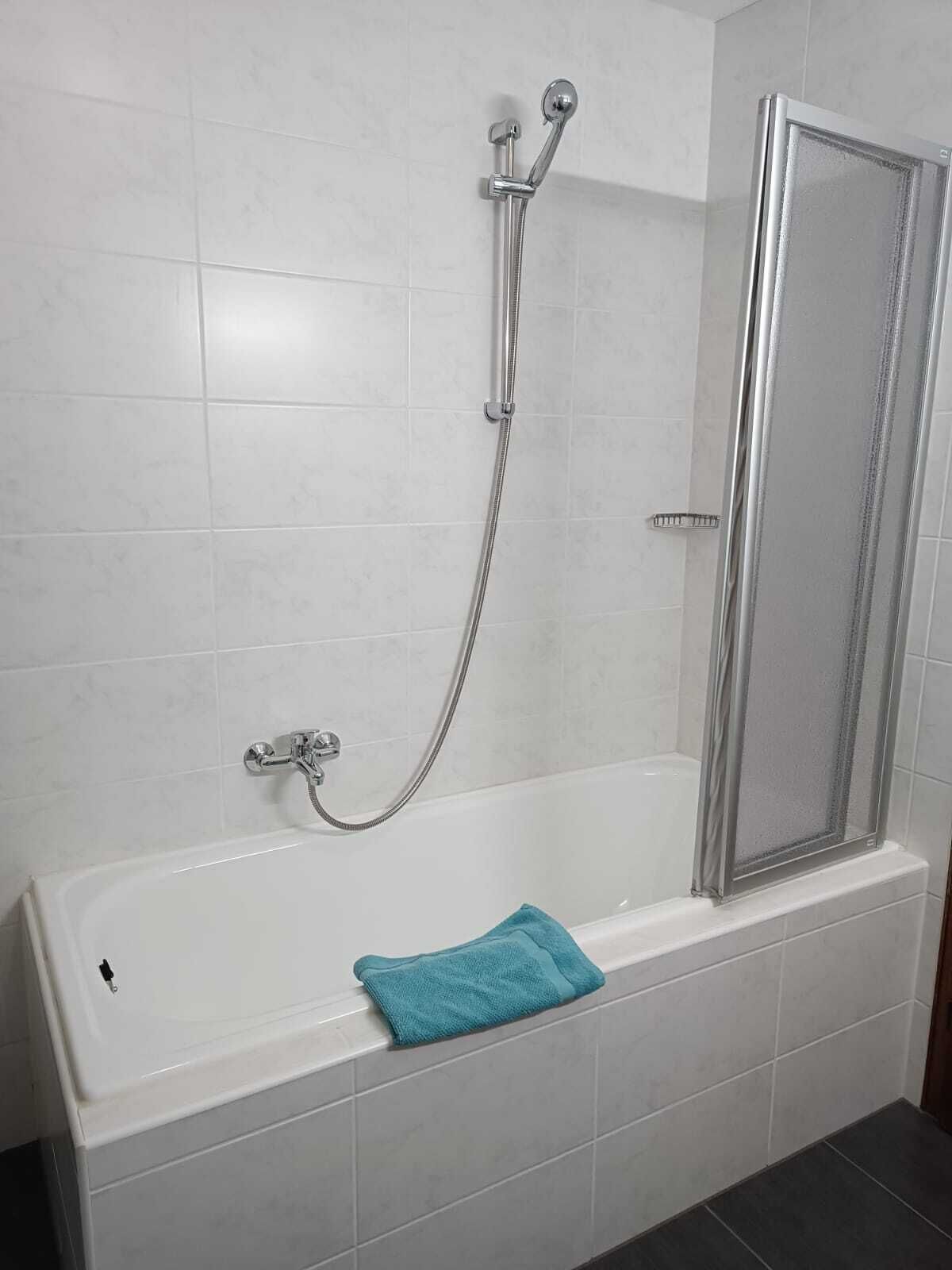 Ein Badezimmer mit einer weißen Badewanne, einer Dusche mit Glastür und einem blauen Handtuch auf der Wanne.
