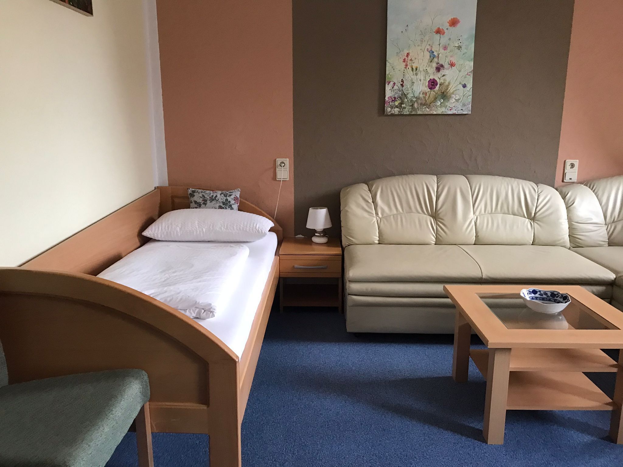 Una habitación de hotel con una cama individual, un sofá, una mesita y un cuadro en la pared.