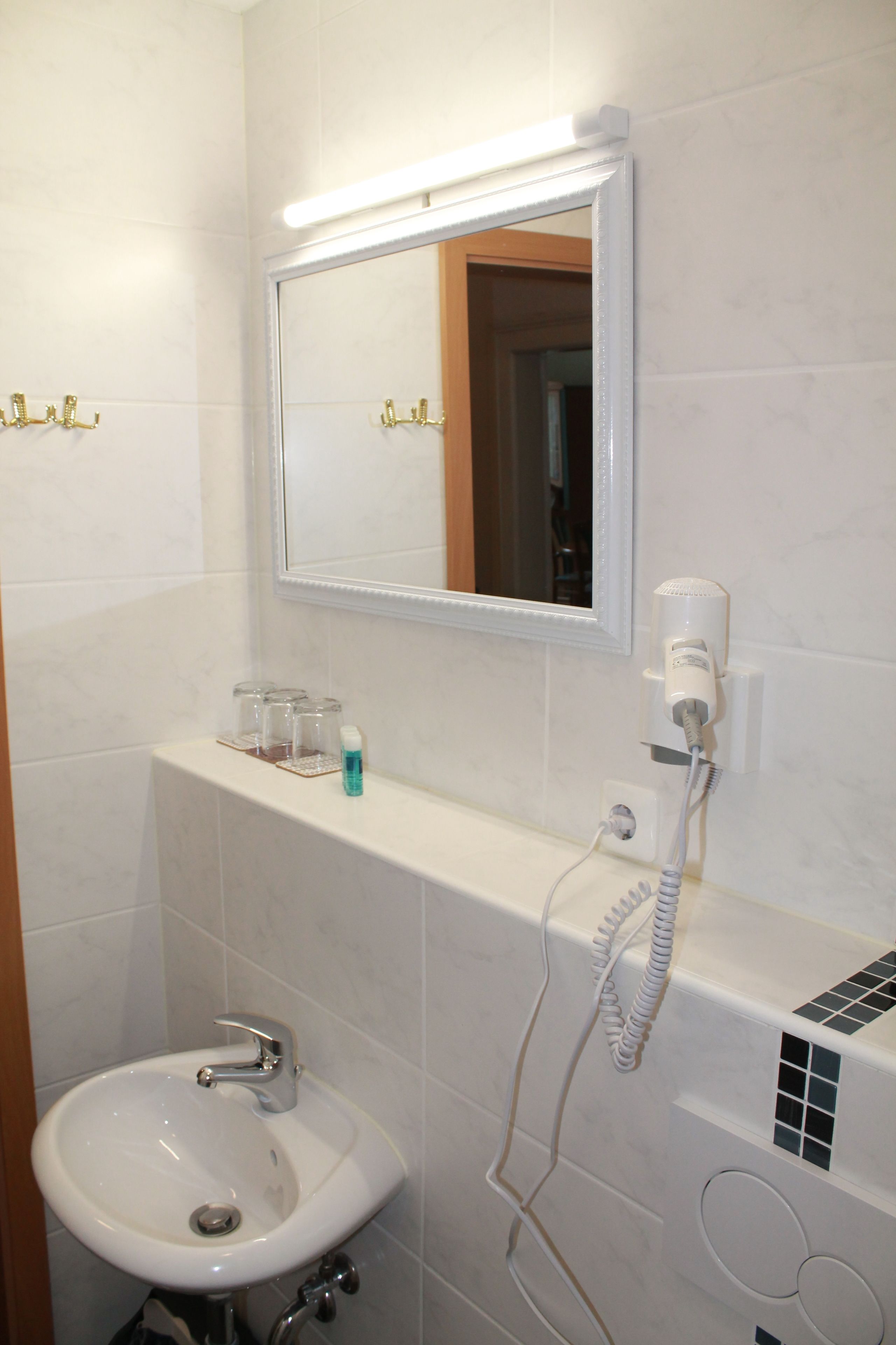 Une salle de bain avec un lavabo blanc, un miroir et un sèche-cheveux fixé au mur.