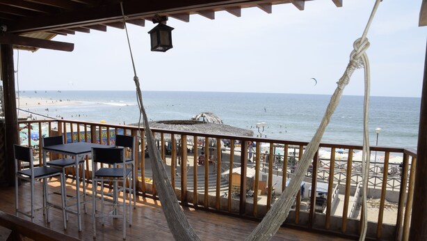 Une terrasse en bois avec un hamac, des tables et des chaises, donnant sur une plage.