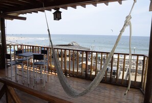 A wooden deck with a hammock, tables, and chairs overlooking a beach. - La Pachamama (Máncora)