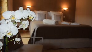 Habitación de hotel con cama, almohadas y un jarrón de orquídeas blancas.