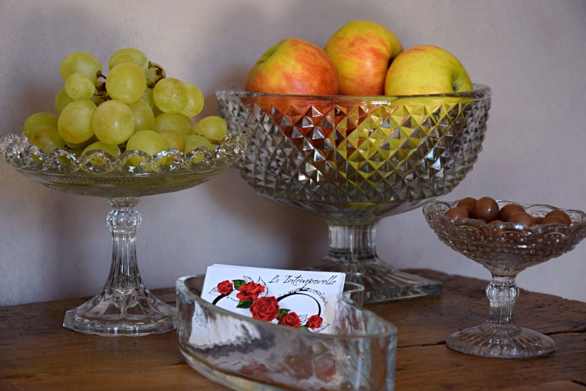 Três tigelas de vidro sobre uma mesa de madeira, cada uma com frutas diferentes.