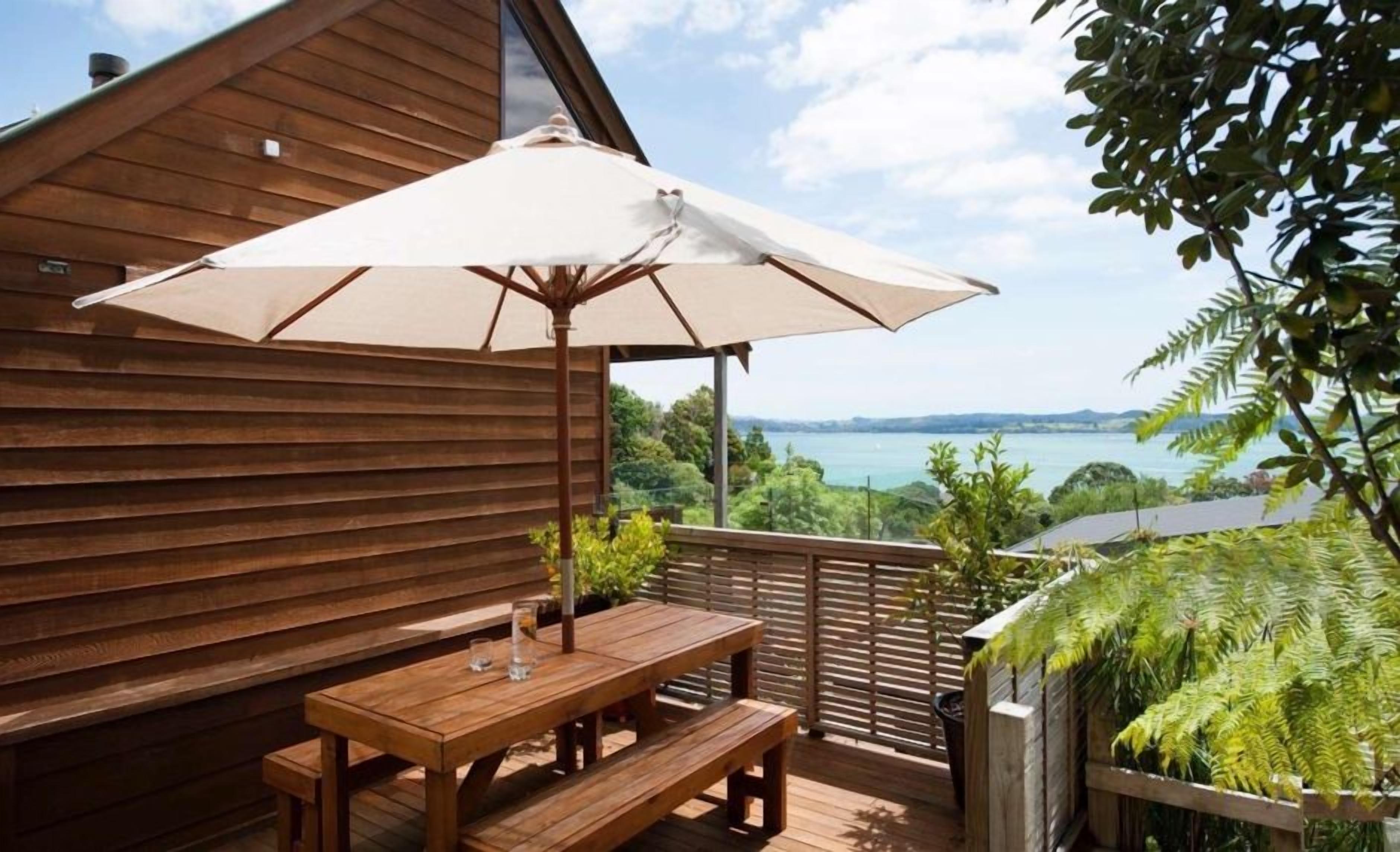A wooden deck with a table and bench, an umbrella, and a view of the sea.