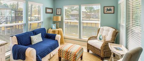 A cozy room with a blue quilted sofa, a wicker chair, and a patterned ottoman.