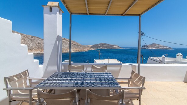 A terrace with a table and chairs, overlooking a coastal landscape with clear blue sea and distant islands. - House with character (Tinos)