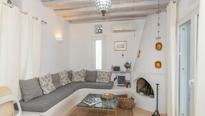 A cozy living room with a curved grey sofa, a small coffee table, and a fireplace. - House with character (Tinos)