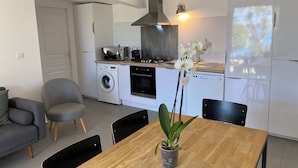 Une cuisine moderne équipée d’un lave-linge, d’une cuisinière et d’un évier. On y trouve une table à manger avec des chaises et un pot d’orchidée.
