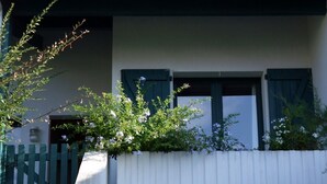 Un bâtiment à l’extérieur blanc, avec des volets verts et une clôture en bois peinte en blanc.
