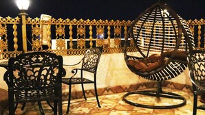Una terraza con barandillas de metal ornamentales, un sillón colgante y dos sillas con diseños elaborados.