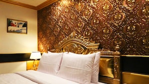 Una habitación de hotel con una cama grande, un cabecero dorado, un teléfono en la mesita de noche y un cuadro en la pared.